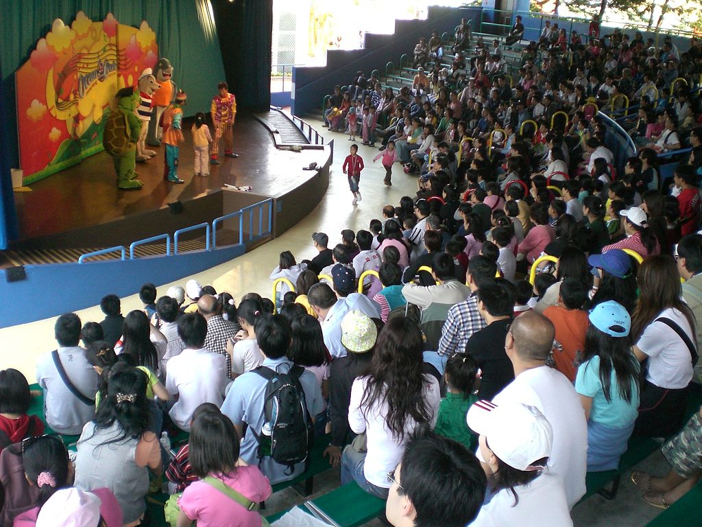 A photograph of an audience at a stage show featuring actors dressed as cartoonish animals.