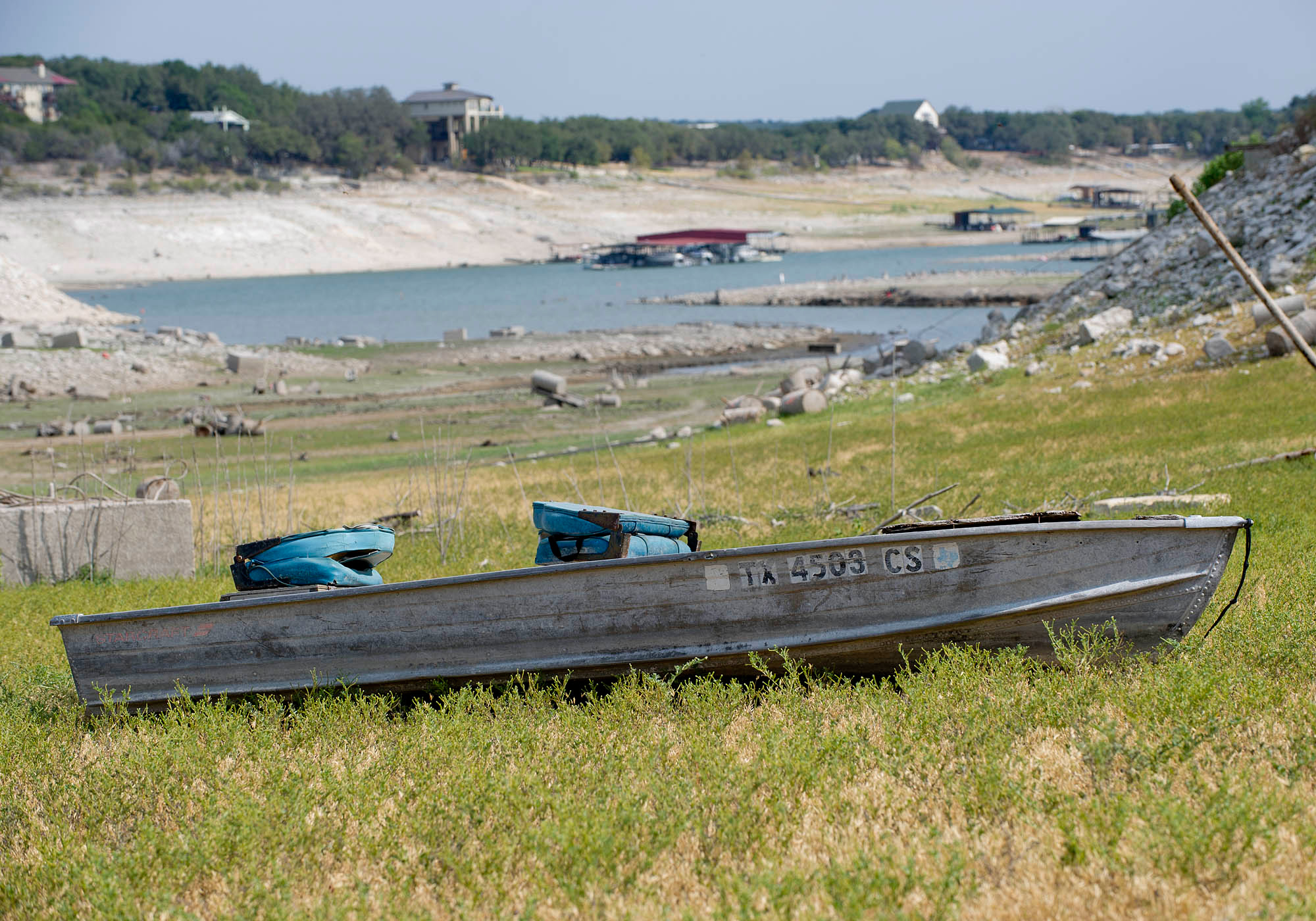 Photo of the dry basin of Lake Travis, near Austin. While there is some water in the bottom of the lake, the picture focuses on a boat that is grounded on a grassy plain.