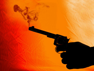 A silhouette photograph of a hand holding a smoking pistol