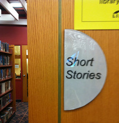 A photograph of the Short Stories section of a library. There is a sign on the side of the bookshelf that reads; Short Stories.