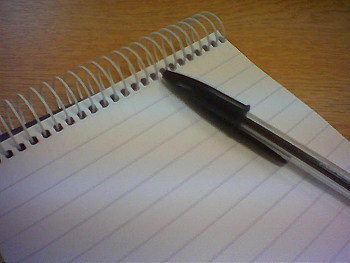 A pen laying on a on a blank sheet of paper in a spiral notebook