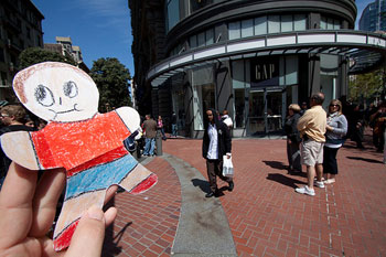 A photograph of a ‘Flat Stanley’ outside of a GAP store in an outdoor shopping area.