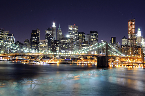 A photograph of downtown New York City (Manhattan) at night taken from the opposite side of the Manhattan bridge.