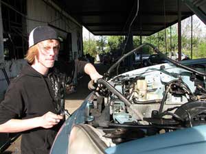 A photograph of a young man working on a car engine in a garage 