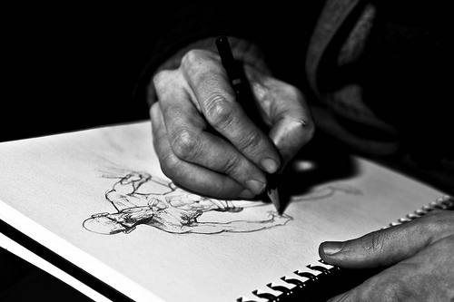 A photograph of a person’s hand sketching out a comic book style character