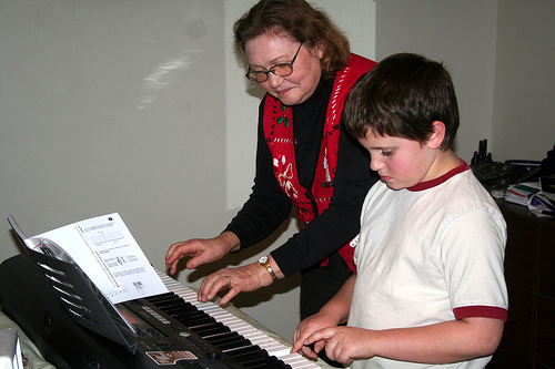 An older woman gives a child piano lessons on a synthesizer keyboard.