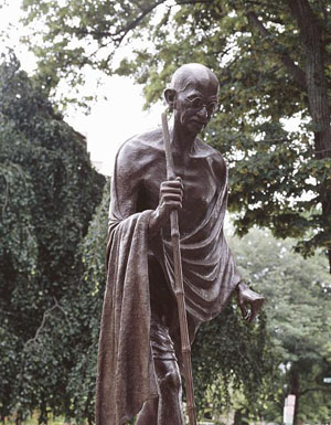 photo of bronze Ghandi sculpture; he walks with a stick, wears glasses, and is wrapped in a robe