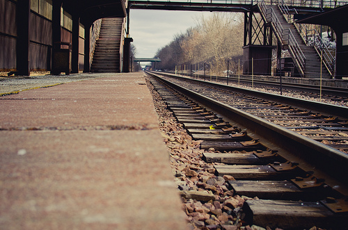 Parallel radio tracks extend toward the horizon in a photograph taken from a run-down train station.