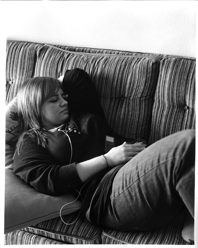 black and white photo of teenage girl reclined on a sofa listen to music through an iPod