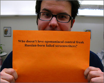 A man holding a sign that reads “Who doesn’t love egomaniacal control freak Russian-born failed screenwriters?“