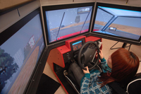 Photo of a girl learning to drive in a driving simulator with three screens