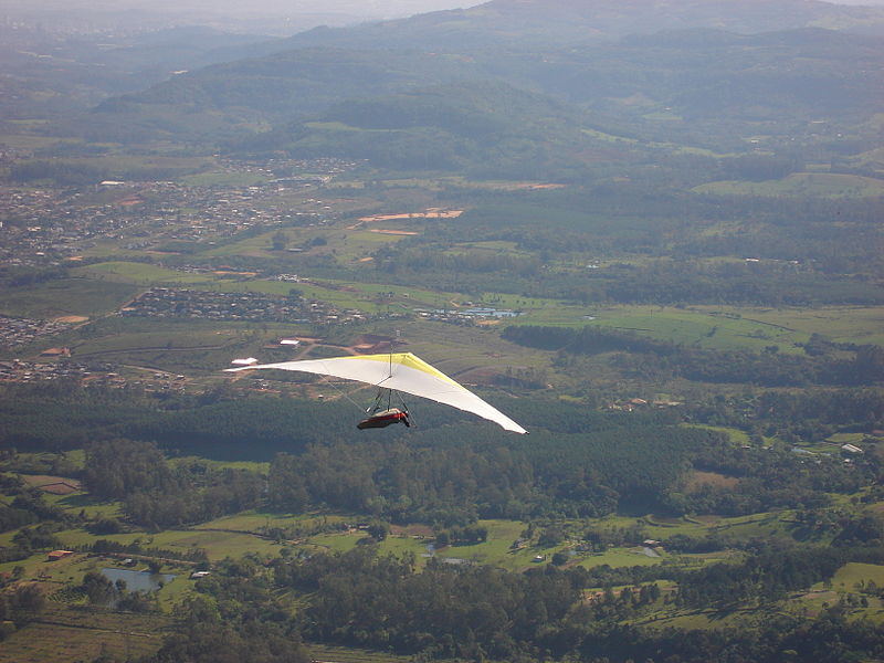 A photograph of a single hang glider soaring over the countryside