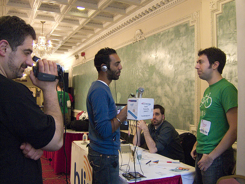 A photograph of a young man being interviewed. The interviewer is holding a microphone; There is camera man behind him.