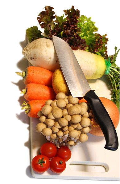A photograph of a chopping board with various vegetables on it. There is a chopping knife laying on the vegetables.