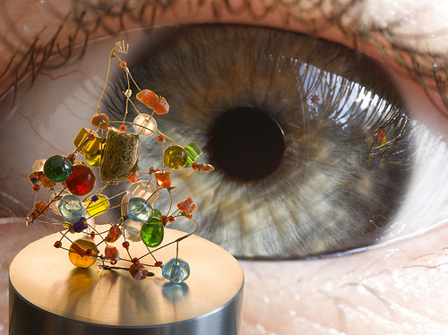 An up close photograph of a person’s eye looking at a small, intricately constructed piece of art