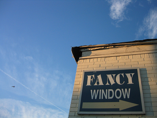A photograph of a sign on the corner of a building that reads “Fancy Window” with a right pointing arrow
