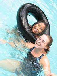 A photograph of a lifeguard water instructor in the pool with another girl who is learning to swim