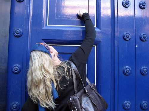 A photograph of a girl knocking on a large wooden door.