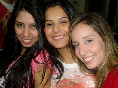 A photograph of three female friends standing close together and smiling at the camera