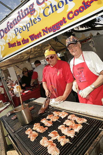 photo of two men in aprons cooking chicken behind a huge grill