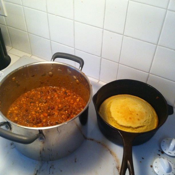 A photograph of home-made cornbread in a skillet and Texas chili in a pot on a countertop.
