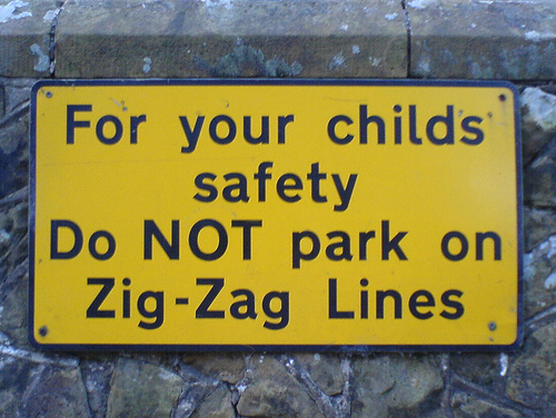 photo a yellow that sign that reads “For your child’s safety Do NOT park on Zig-Zag Lines”; capitalization is very inconsistent.