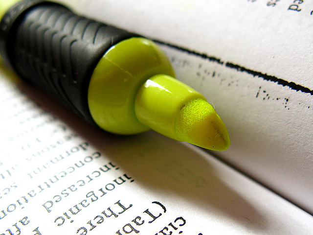 a yellow highlighter with a very sturdy grip resting in the crook of an open book