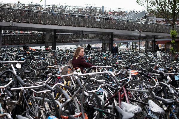 One woman confounded in a sea of bikes; it is as if she searches for her bike, bike chain, or a place to put her bike.