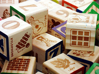 A photograph of blocks, the kind a child would play with. One side has a letter, and the other sides have numbers and various nouns/items.