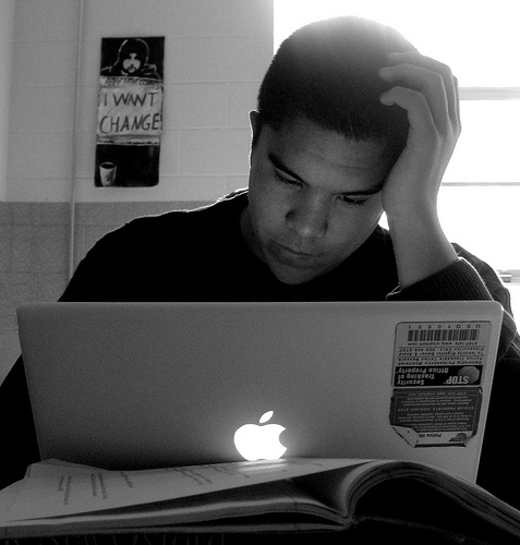 A photograph of a young man studying with a laptop computer open in front of him