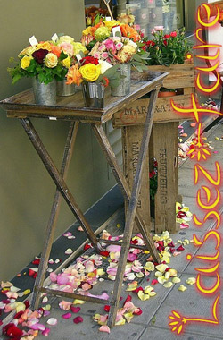 A sidewalk flower sale in front of a florist’s shop. Petals are scattered around the ground in a carefree manner.