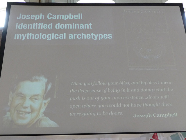 An image of Joseph Campbell on a slide. The top reads “Joseph Campbell identified dominant mythological archetypes.” The bottom right reads, “When you follow your bliss, and by bliss I mean the deep sense of being in it and doing what the push is out of your own existence . . . doors will open where you would not have thought there were going to be doors.” –Joseph Campbell