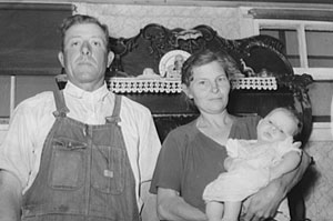 A black and white photo of farmer and his wife proudly holding their new baby.