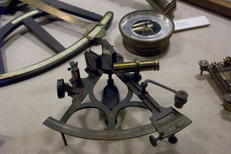 A collection of nautical navigation instruments including a sextant and a directional compass.