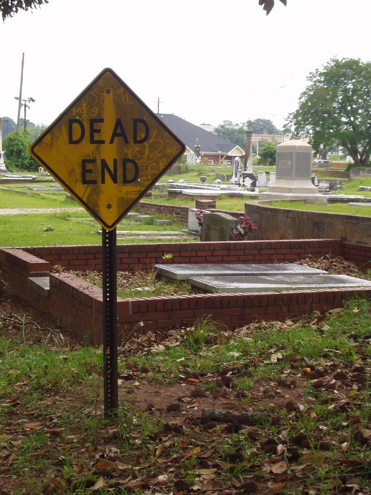 A photograph of a Dead End sign on a street which is located next to a cemetery.