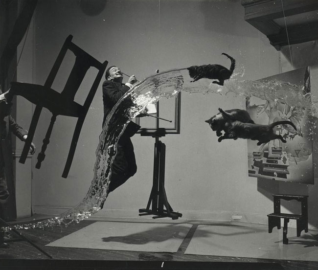 A photograph of painter Salvador Dali in his studio with various objects like water, cats and furniture floating around him.