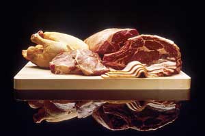 A photograph of a selection of meats on a cutting board. Shown are a chicken, various cuts of beef, pork chops, and bacon.