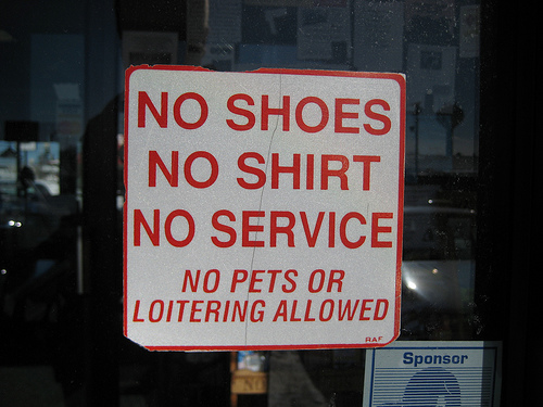 A photograph of a sign that reads “No Shoes, No Shirt, No Service: No Pets or Loitering Allowed.”