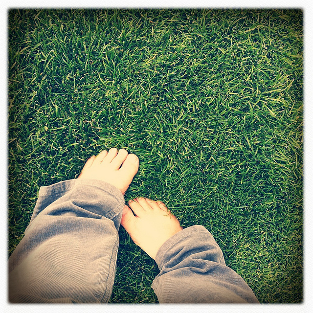 A point of view photograph of a person’s bare feet in the grass.