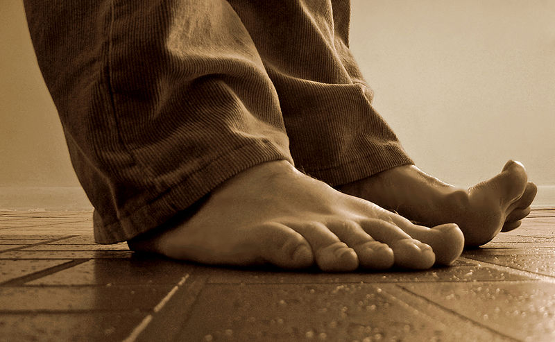 A photograph of a person’s bare feet standing on a floor taken from the angle of the floor.