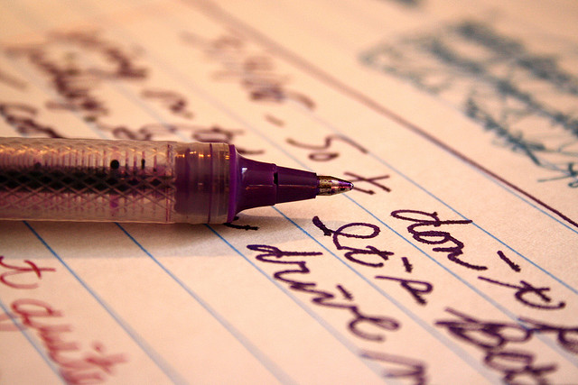 A photograph of a pen laying on a sheet of paper that has lines of cursive text on it.