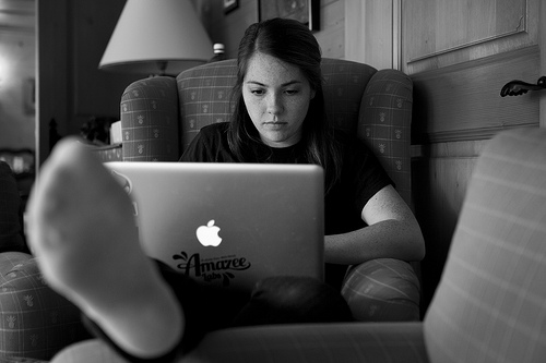 A photograph of a girl sitting in a chair, concentrating on her laptop computer screen.