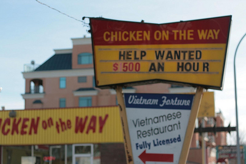 A photograph of a Chicken on the Way sign advertising “Help Wanted: $5.00 an Hour.”
