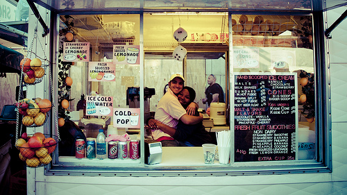 A photograph of two young workers embracing in a snak trailer service window.