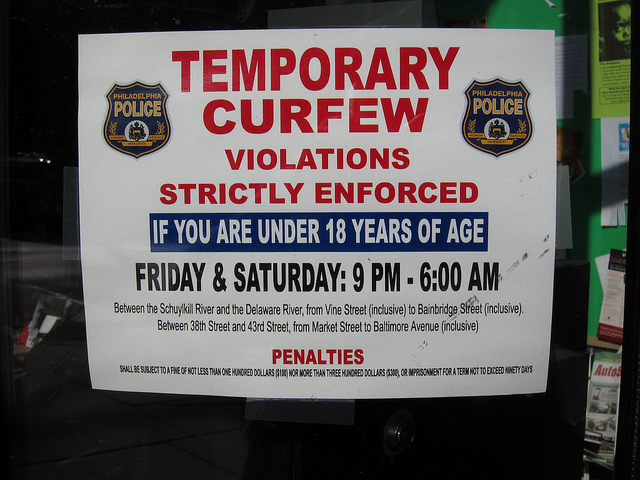 A sign put up by the Philadelphia Police reminding those under 18 years of age that there is a temporary curfew Friday and Saturday nights form 9:00 PM until 6:00 AM. The sign also says that violations will be strictly enforced.