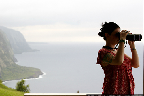 young girl looking through binolculars with a mountainous coast behind her