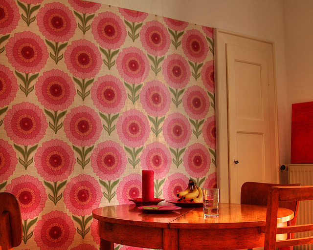 A room with dingy wallpaper that bears a pattern of large, pink flowers