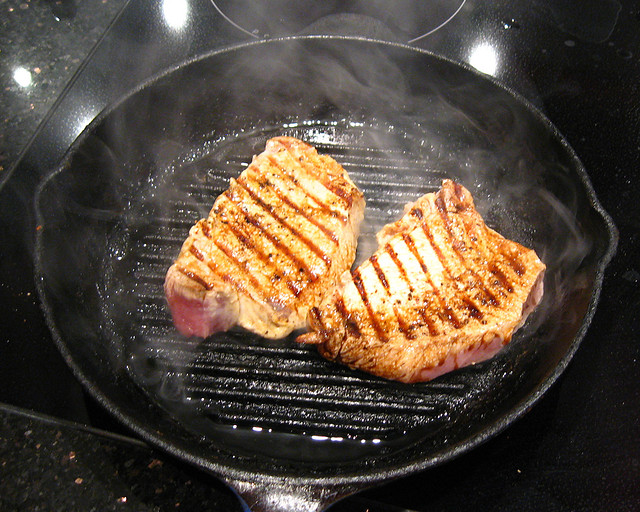Two pork chops frying in an iron skillet