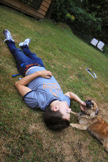photo of a boy lying on the grass as dark nears. He pets a dog that lies near his head.