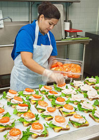 A photograph of a cafeteria worker preparing sandwiches